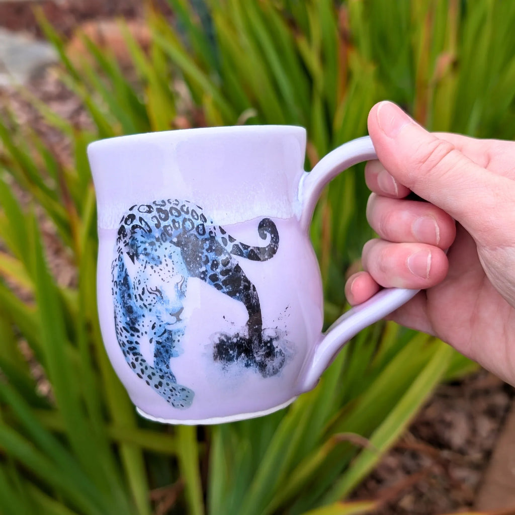 Hand holding a mug with a leopard design against a natural background