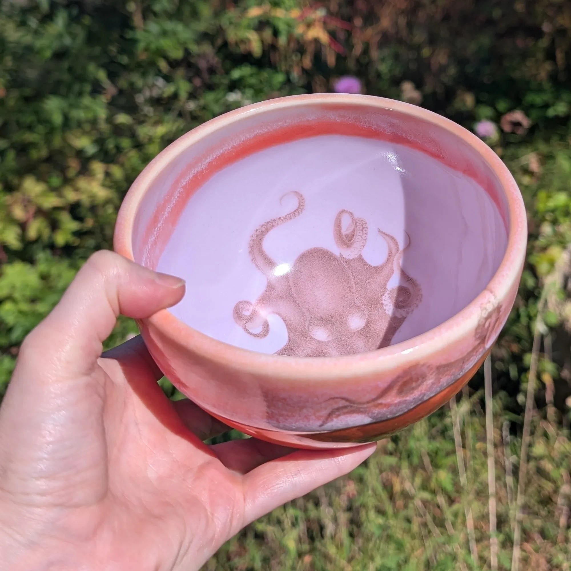 Hand holding a pink ceramic bowl with an octopus design against a natural background